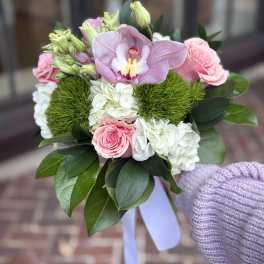 Handheld bouquet of pink orchid, roses, and white hydrangea with green accents and a lavender ribbon.