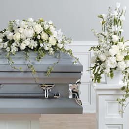 White floral sprays and roses arranged on a gray casket