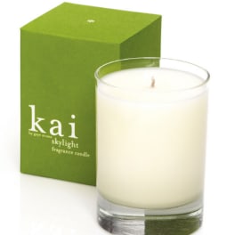 White candle in a clear glass tumbler beside a green box