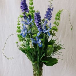Tall blue and purple floral arrangement in a clear glass vase