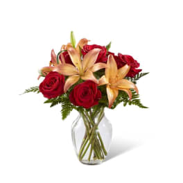 Red roses and peach lilies in a clear glass vase