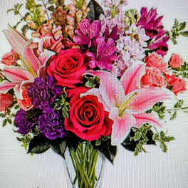 Mixed bouquet of pink lilies, roses, and purple flowers in a clear vase