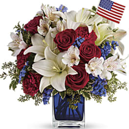 Red roses and white lilies in a blue glass vase with a small American flag