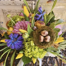 Mixed bouquet with purple and pink flowers, yellow tulips, and a bird nest centerpiece
