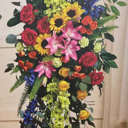 Tall standing floral spray with roses, lilies, sunflowers, and blue flowers