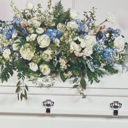 White and blue floral arrangement in a white casket