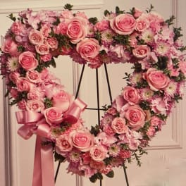 Heart-shaped pink rose and mixed flower wreath on a stand with a satin ribbon