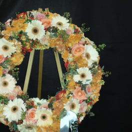 Floral wreath with white daisies, peach roses, and orange blooms on a stand
