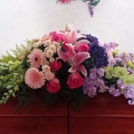 Casket spray with pink lilies, roses, and purple flowers