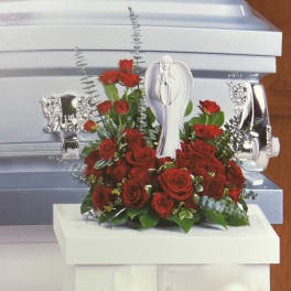 Red roses arranged around a white angel figurine on a casket