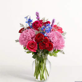 Bouquet of pink, red, and blue flowers in a clear glass vase