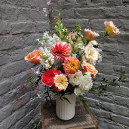 Mixed bouquet of coral, peach, and white flowers in a white vase