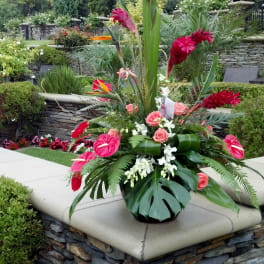 Tall tropical floral arrangement with red blooms and pink roses in a black vase