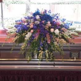 Large floral spray on a casket with blue, purple, pink, and white flowers