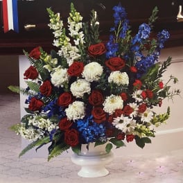 Large red, white, and blue floral arrangement in a white pedestal vase