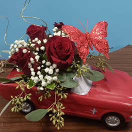 Red roses and baby's breath arranged on a red toy car with a pink butterfly