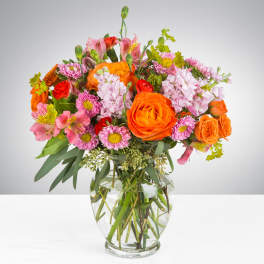 Mixed bouquet of orange, pink, and red flowers in a clear glass vase