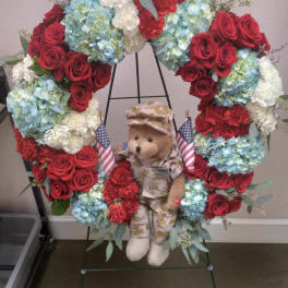 Heart-shaped floral wreath with roses, hydrangeas, and a teddy bear in military uniform