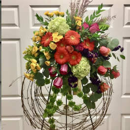 Large mixed floral arrangement on a wire stand with bright roses and gerberas