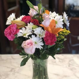 Mixed bouquet of pink roses, lilies, carnations, and white daisies in a glass vase