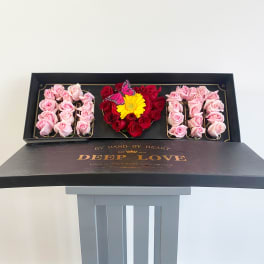 Heart-shaped rose box with pink and red roses and a yellow flower