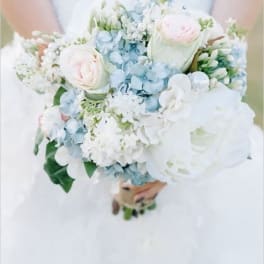 Bride holding a pastel bouquet of white, blue, and pale pink flowers