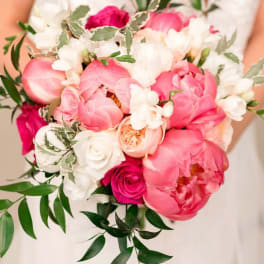 Handheld bouquet of pink and white flowers with trailing greenery