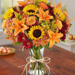 Bouquet of sunflowers, orange lilies, and roses in a glass vase