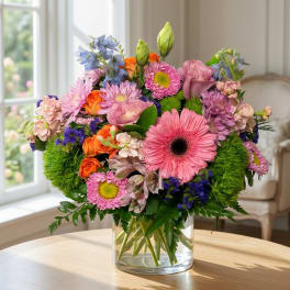 Mixed bouquet of pink, purple, orange, and blue flowers in a clear glass vase