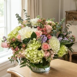 Pastel bouquet of roses, hydrangeas, and white dahlias in a clear glass vase.