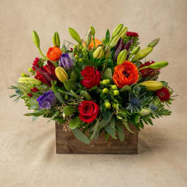 Mixed bouquet in a wooden box with red roses, orange ranunculus, lilies, and purple blooms