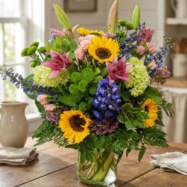Mixed bouquet with sunflowers, lilies, roses, and blue flowers in a glass vase
