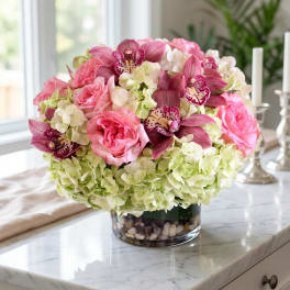 Pink roses and orchids arranged in a glass vase with pale hydrangeas