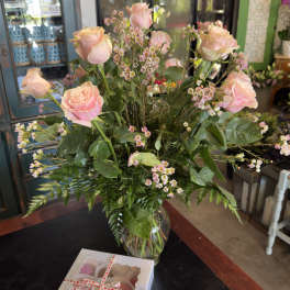 Pink roses and tiny pink filler flowers in a glass vase with a box of chocolates
