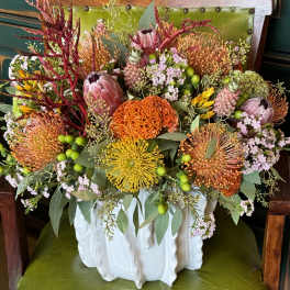 Mixed bouquet in a white ceramic vase with orange, yellow, pink, and green blooms
