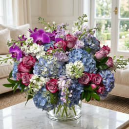 Bouquet of blue hydrangeas, pink roses, and purple orchids in a glass vase