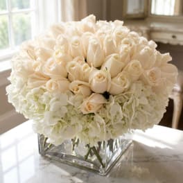 Cream rose bouquet with white hydrangeas in a clear square vase