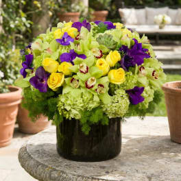 Round bouquet of yellow roses, purple orchids, and green blooms in a dark vase