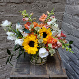 Mixed bouquet with sunflowers, white blooms, and orange flowers in a glass vase