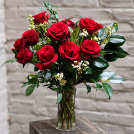 Red roses arranged in a clear glass vase with small white filler flowers