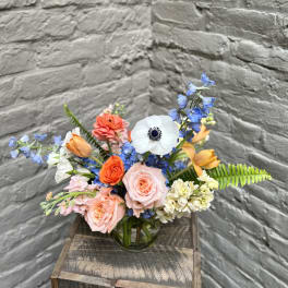 Mixed bouquet of roses, tulips, and blue flowers in a glass vase
