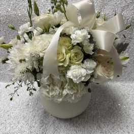 White floral arrangement with roses, carnations, and a satin ribbon in a vase
