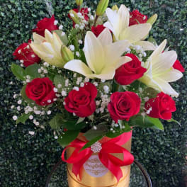 Bouquet of red roses and white lilies in a gold box with a red ribbon