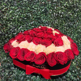 Red and cream roses arranged in a round black box with a red ribbon
