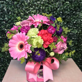 Pink and purple mixed flower arrangement in a pink box with a ribbon