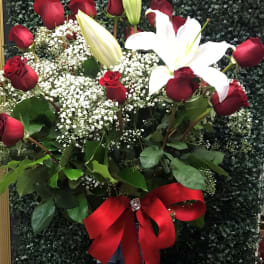 Red roses and white lilies in a clear vase with a red ribbon