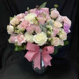 Pink and white rose bouquet in a black vase with a pink ribbon