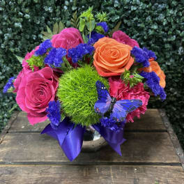 Bright mixed rose arrangement with purple accents in a vase