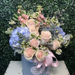 Pastel bouquet of roses, hydrangeas, and small white blooms in a blue hat box