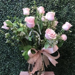 Pink roses arranged in a patterned vase with a pink ribbon bow